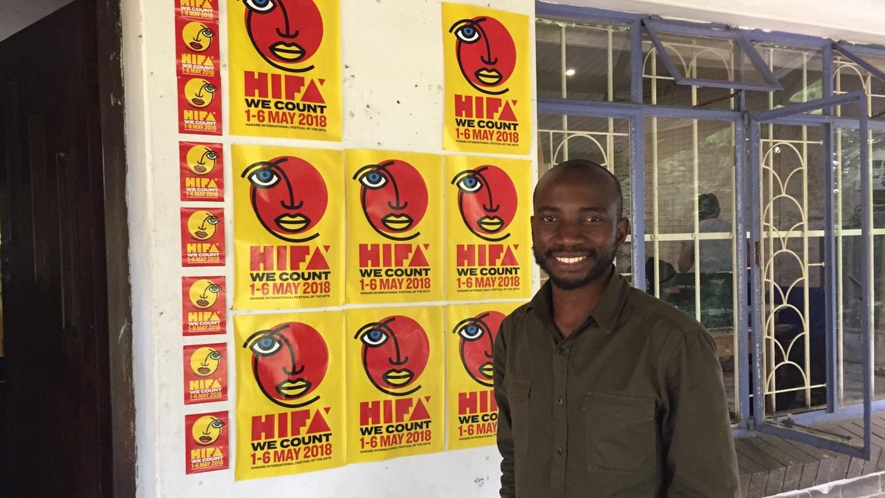 Tafadzwa Simba, stellvertretender Direktor des Hifa Festivals, steht in Simbabwes Hauptstadt Harare vor einer Häuserwand,die mit Plakaten zum Kulturfestival beklebt ist.