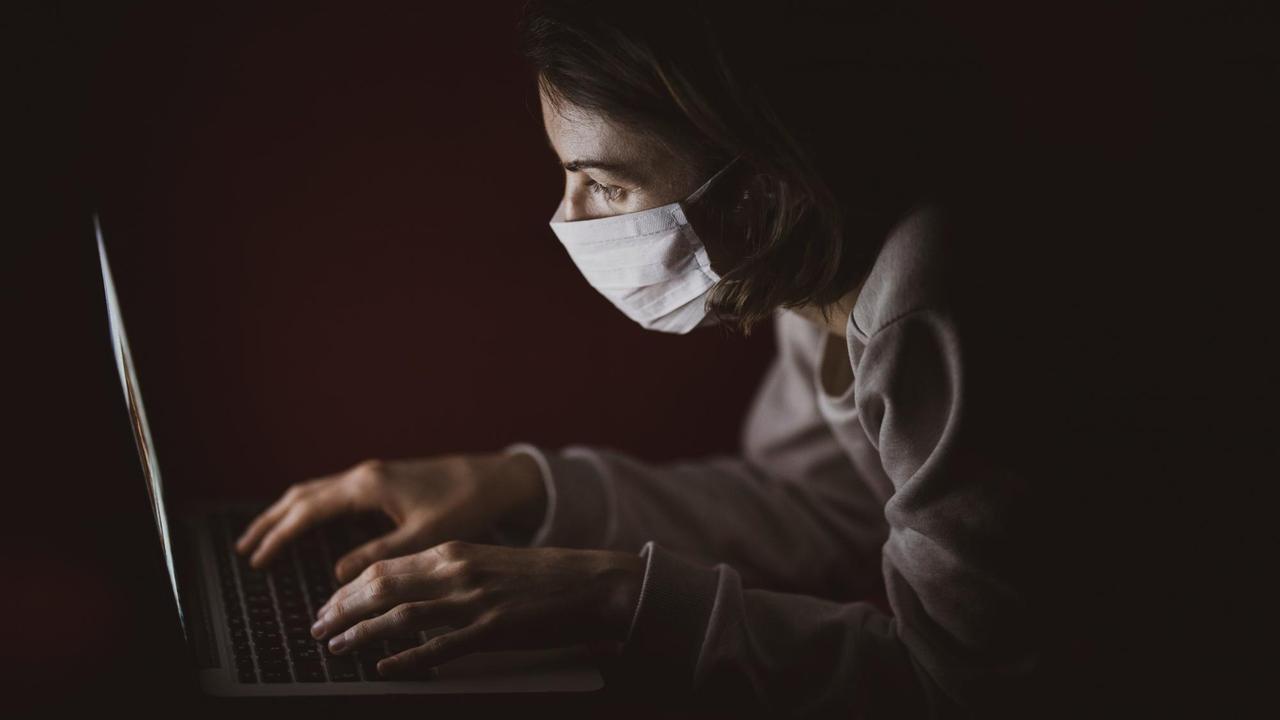 Eine Frau sitzt mit Atemschutzmaske vor ihrem Laptop. Eine Frau sitzt mit Atemschutzmaske vor ihrem Laptop.