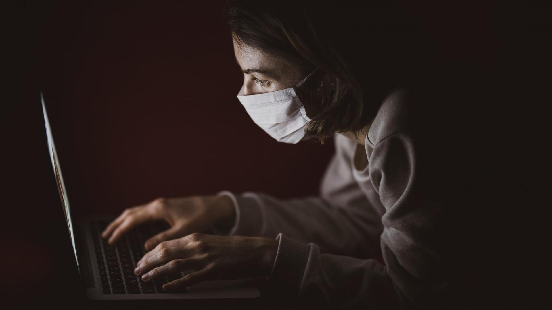 Eine Frau sitzt mit Atemschutzmaske vor ihrem Laptop. Eine Frau sitzt mit Atemschutzmaske vor ihrem Laptop.