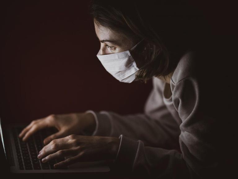 Eine Frau sitzt mit Atemschutzmaske vor ihrem Laptop.