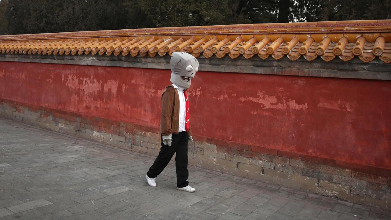 Ein chinesischer Schauspieler geht, als Zombie verkleidet, an einer Tempelmauer entlang Ein chinesischer Schauspieler geht, als Zombie verkleidet, an einer Tempelmauer entlang