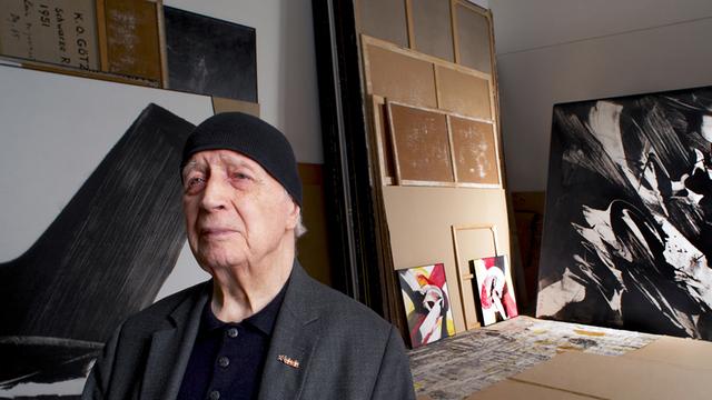 Karl Otto Götz im Alter von 85 Jahren in einem Atelier, im Hintergrund einige Gemälde.