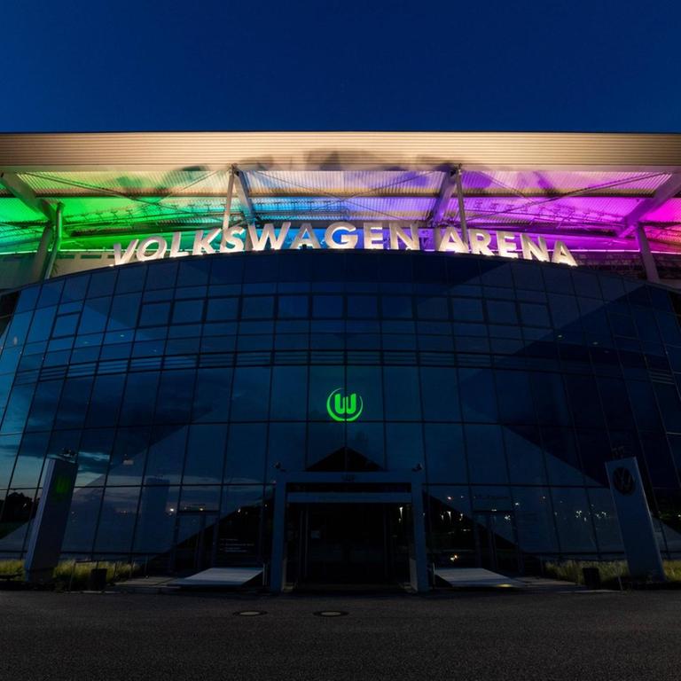 Das Stadion des VfL Wolfsburg erstrahlt vor einem dunklen Himmel in Regenbogenfarben.