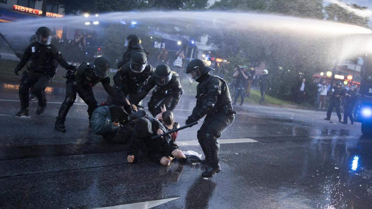 Ein Polizist schlägt mit einem Schlagstock auf Demonstranten beim G20-Gipfel 2017 in Hamburg ein, andere Polizisten halten die Protestierenden fest Ein Polizist schlägt mit einem Schlagstock auf Demonstranten beim G20-Gipfel 2017 in Hamburg ein, andere Polizisten halten die Protestierenden fest