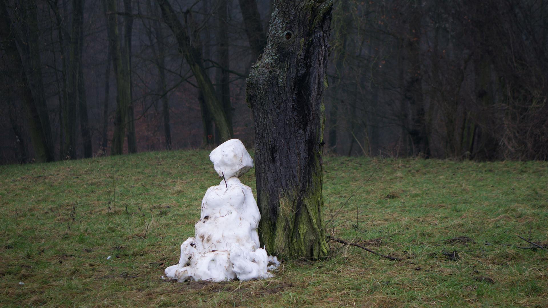 Ein dahinschmelzender Schneemann steht an einem Waldrand auf einer grünen Wiese. Ein dahinschmelzender Schneemann steht an einem Waldrand auf einer grünen Wiese.