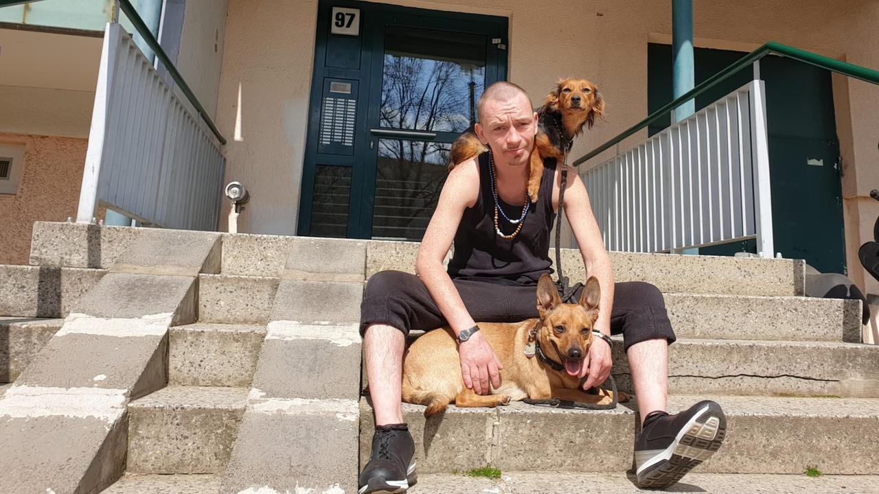 Benjamin ist 35 Jahre alt und sitzt mit seinen Hunden auf den Treppen des Hauseingangs seiner Wohnung in Berlin. Benjamin ist 35 Jahre alt und sitzt mit seinen Hunden auf den Treppen des Hauseingangs seiner Wohnung in Berlin.