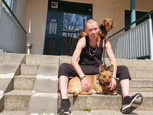 Benjamin ist 35 Jahre alt und sitzt mit seinen Hunden auf den Treppen des Hauseingangs seiner Wohnung in Berlin.