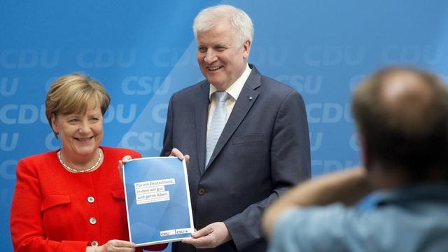 Merkel und Seehofer mit Parteigrogramm vor Kameras