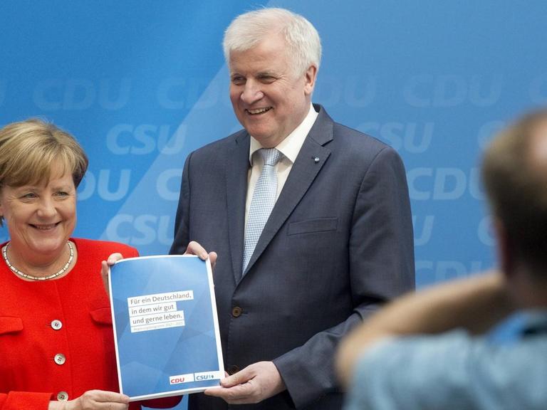 Merkel und Seehofer mit Parteigrogramm vor Kameras