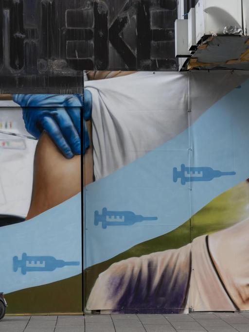Wandbild an einem leerstehenden Geschäftsgebäude, das die Corona Krise thematisiert, das Impfen und die Freiheiten nach dem Impfen. Abgebildet ist ein Arm der geimpft wird und eine Frau die Eis isst.