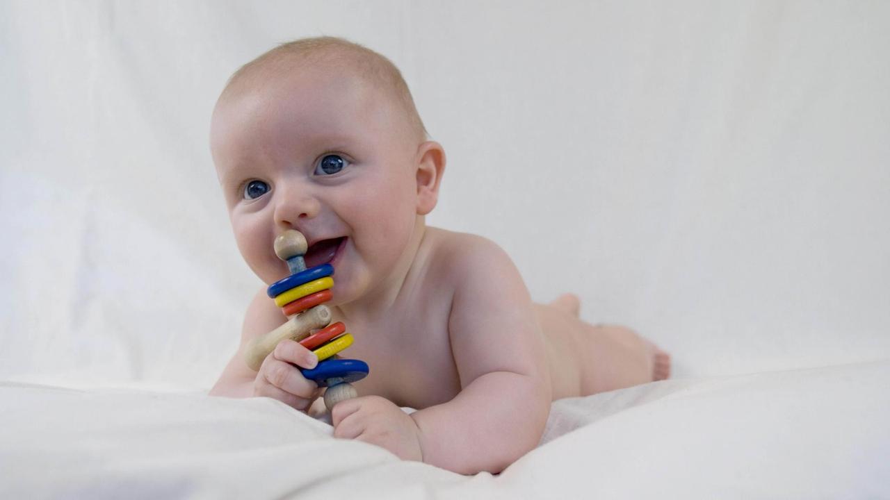Baby, auf dem Bauch liegend, mit Rassel Baby, auf dem Bauch liegend, mit Rassel