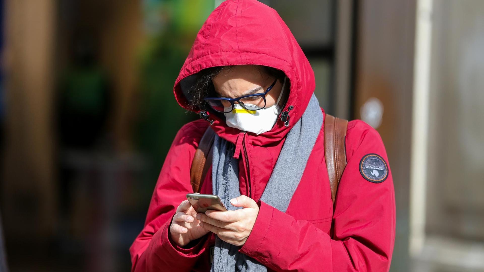 Ein Mann in London mit einer Schutzmaske am 11. März 2020 blickt auf sein Smartphone. Ein Mann in London mit einer Schutzmaske am 11. März 2020 blickt auf sein Smartphone.