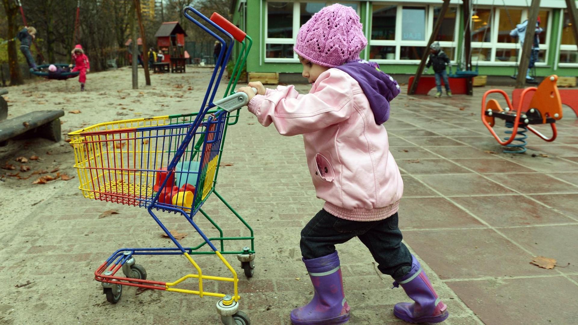 Ein Kind schiebt einen Kinder-Einkaufswagen über einen Spielplatz. Ein Kind schiebt einen Kinder-Einkaufswagen über einen Spielplatz.