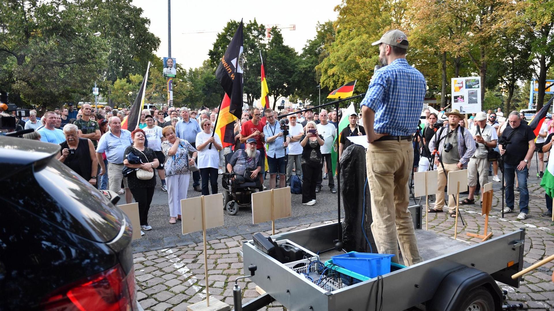 Das Bild zeigt Menschen mit Deutschland-Fahnen, die vor einem Redner stehen. Das Bild zeigt Menschen mit Deutschland-Fahnen, die vor einem Redner stehen.