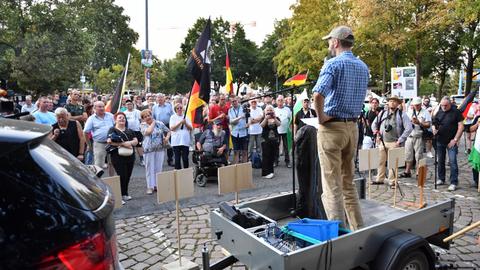 Das Bild zeigt Menschen mit Deutschland-Fahnen, die vor einem Redner stehen.
