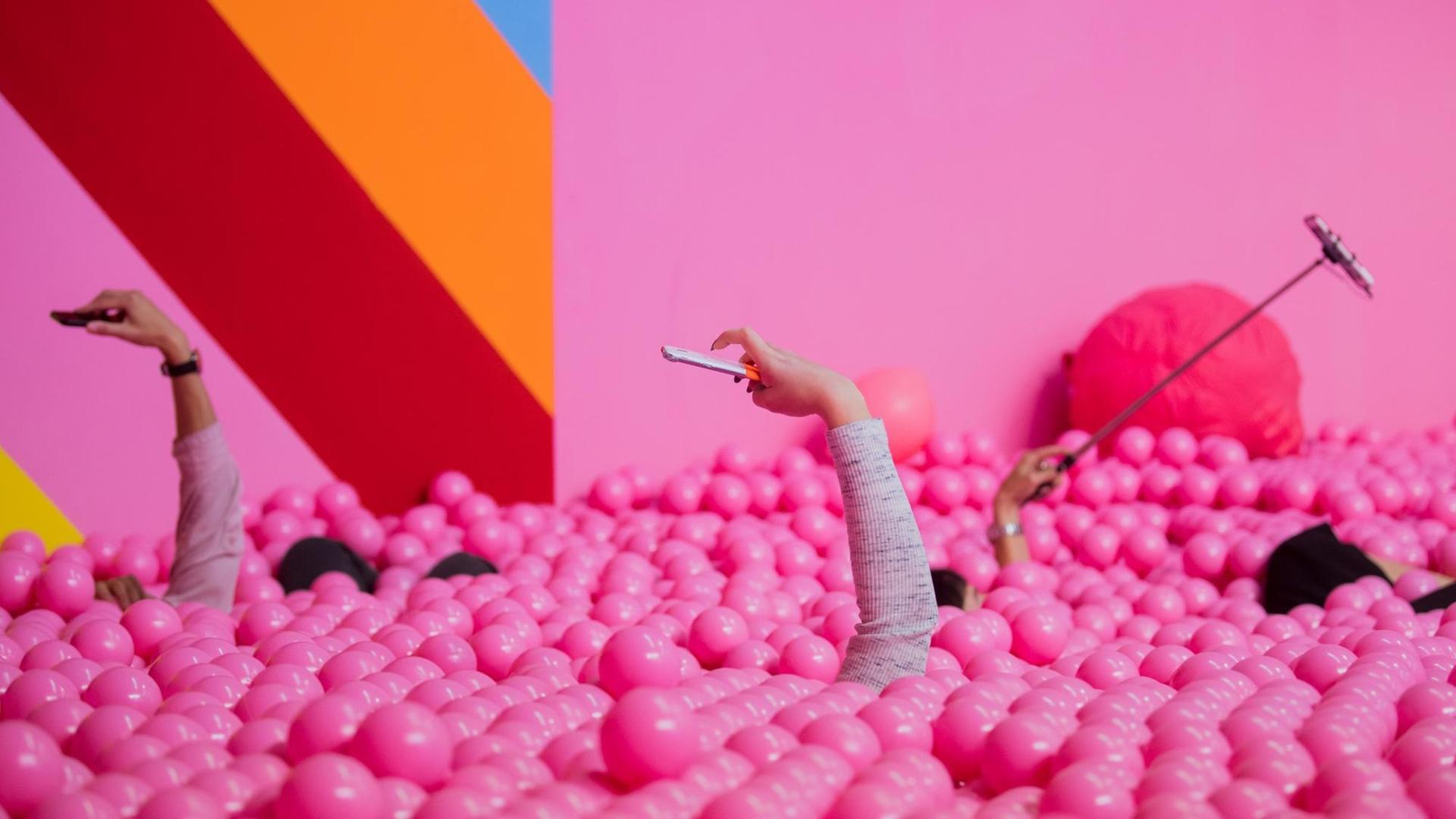 Besucherinnen machen im Supercandy Pop-Up Museum in einem Bällchenbad Selfies. Besucherinnen machen im Supercandy Pop-Up Museum in einem Bällchenbad Selfies.