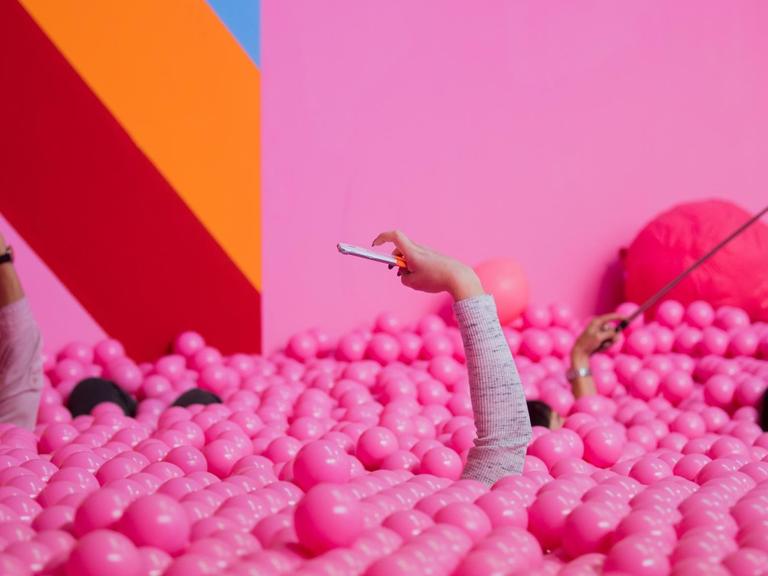 Besucherinnen machen im Supercandy Pop-Up Museum in einem Bällchenbad Selfies.
