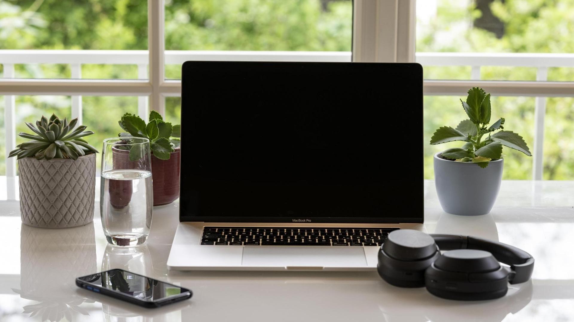 Schreibtisch mit Laptop, Telefon und mit Kopfhörern am Schreibtisch vor einem Fenster. Schreibtisch mit Laptop, Telefon und mit Kopfhörern am Schreibtisch vor einem Fenster.