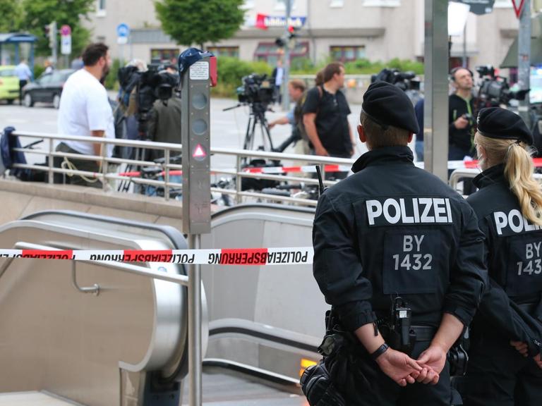 Sie sehen Polizisten und ein Absperrband am Eingang zur U-Bahnstation Olympia-Einkaufszentrum.