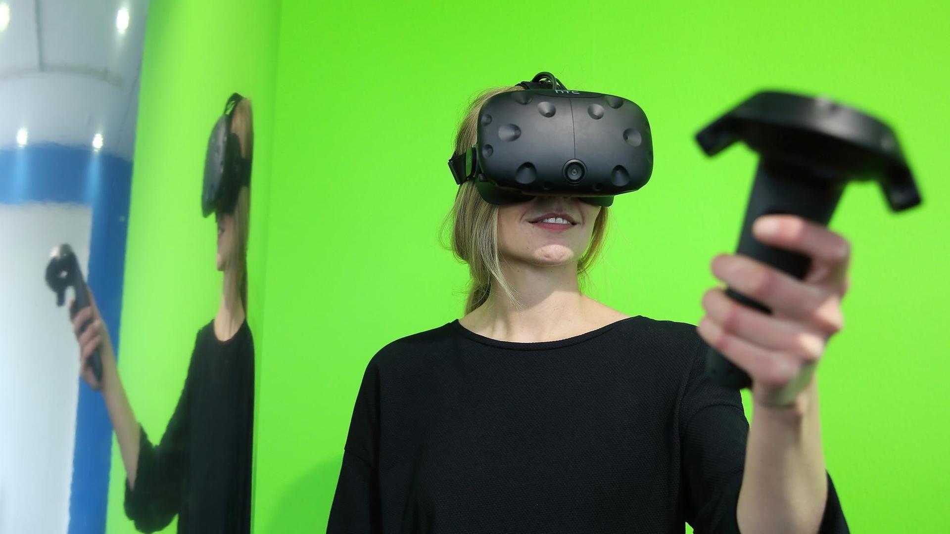 Eine Frau steht am 23.05.2017 im NRW-Forum in Düsseldorf vor einem grünem Hintergrund. Sie trägt eine Virtual-Reality-Brille und hält einen PC Controller, mit dem sie ihre virtuelle-Welt und Erlebnis steuert. Foto: David Young / dpa Eine Frau steht am 23.05.2017 im NRW-Forum in Düsseldorf vor einem grünem Hintergrund. Sie trägt eine Virtual-Reality-Brille und hält einen PC Controller, mit dem sie ihre virtuelle-Welt und Erlebnis steuert. Foto: David Young / dpa