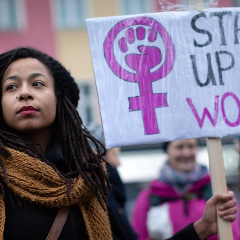 Das Foto zeigt eine junge Demonstrantin auf dem internationalen Frauentag vom 8. März 2019. Sie hält ein Schild mit der Aufschrift: "Stand up for women"