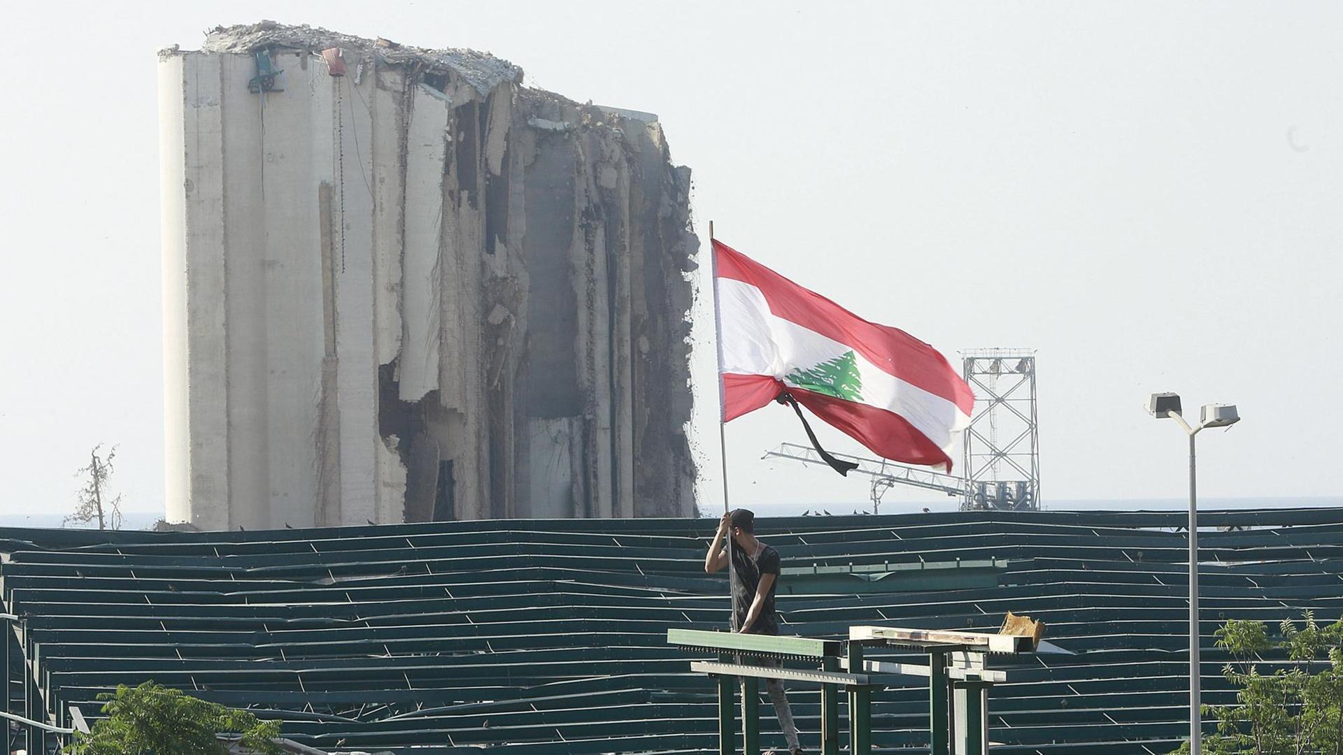 Vor der Kulisse des zerstörten Beiruts hält ein Demonstrant eine libanesische Flagge.