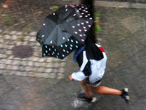 Ein Mann geht mit Schirm auf einem Fußweg durch starken Regen, von oben gesehen