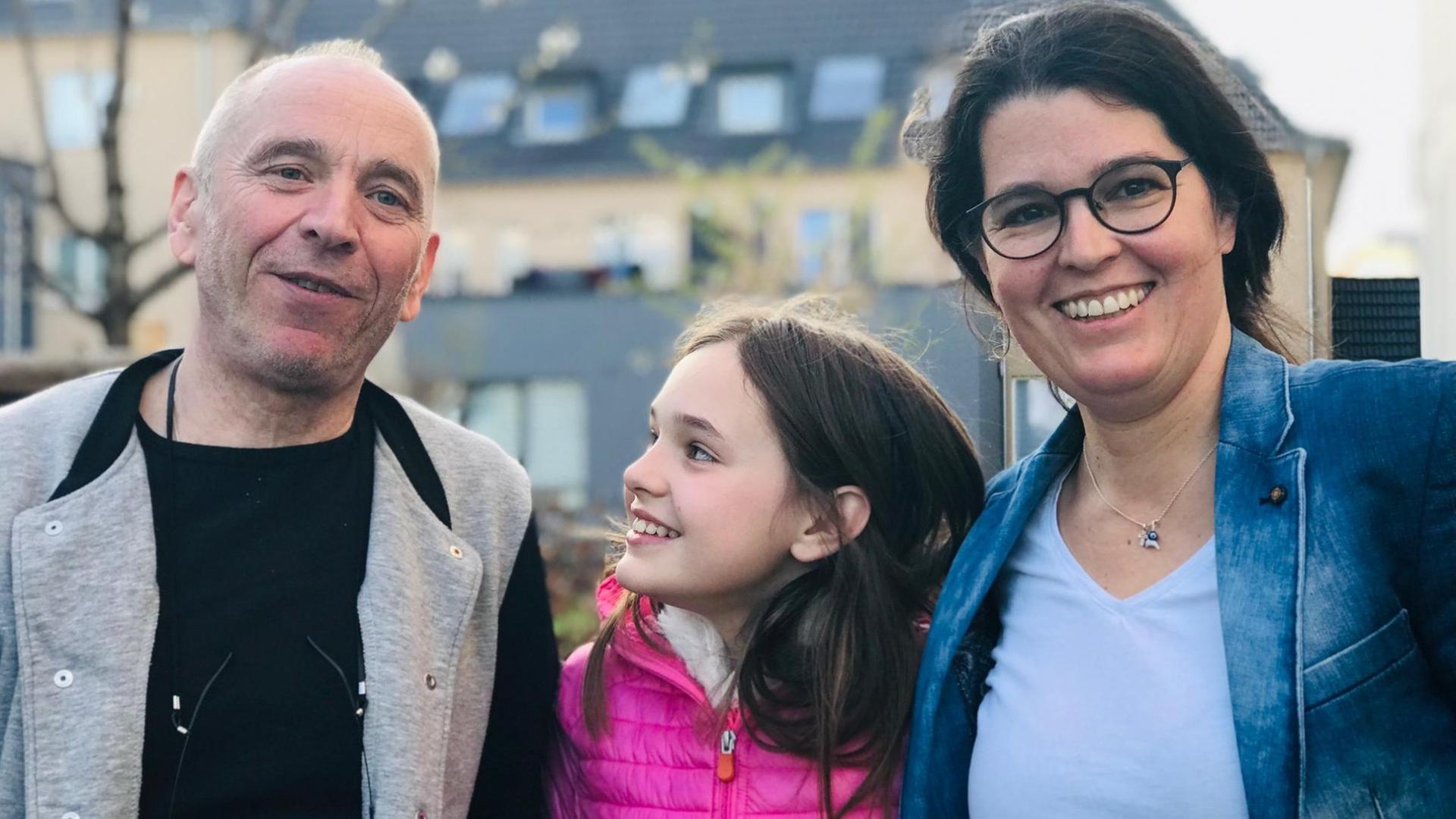 Das Foto zeigt eine lächelnde Familie bestehend aus Mutter, Vater und Tochter. Die Tochter lacht ihren Vater an. Das Foto zeigt eine lächelnde Familie bestehend aus Mutter, Vater und Tochter. Die Tochter lacht ihren Vater an.