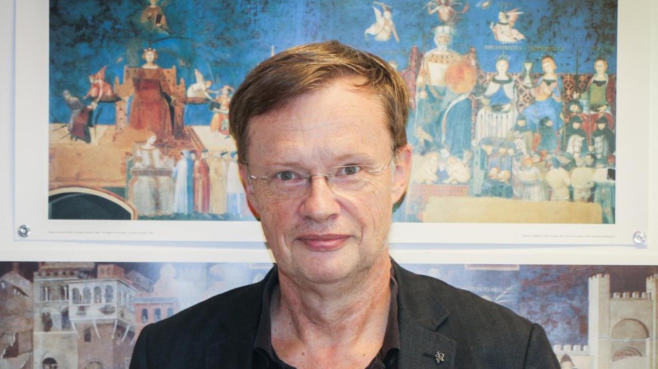 Volker Reinhardt vor religiösen Zeichnungen an einer Wand.