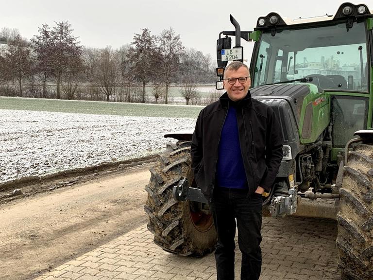 Marcus Arzt ist Ökobauer in Ditzingen und Biolandchef in Baden-Württemberg. Er steht neben seinem schneebedecktem Acker und grünem Traktor im Winter.