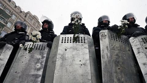 Mit Schilden, Helmen und Schlagstöcken ausgerüstete Polizisten stehen auf einer Straße in Kiew.