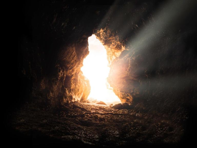 Eingang einer einsamen Höhle, Aufnahme aus dem Inneren. Ein heller Lichtstrahl strömt hinein.