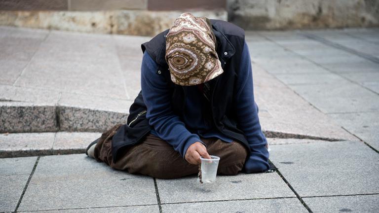Eine Bettlerin in Berlin sitzt mit gesengtem Haupt auf der Straße. Eine Bettlerin in Berlin sitzt mit gesengtem Haupt auf der Straße.