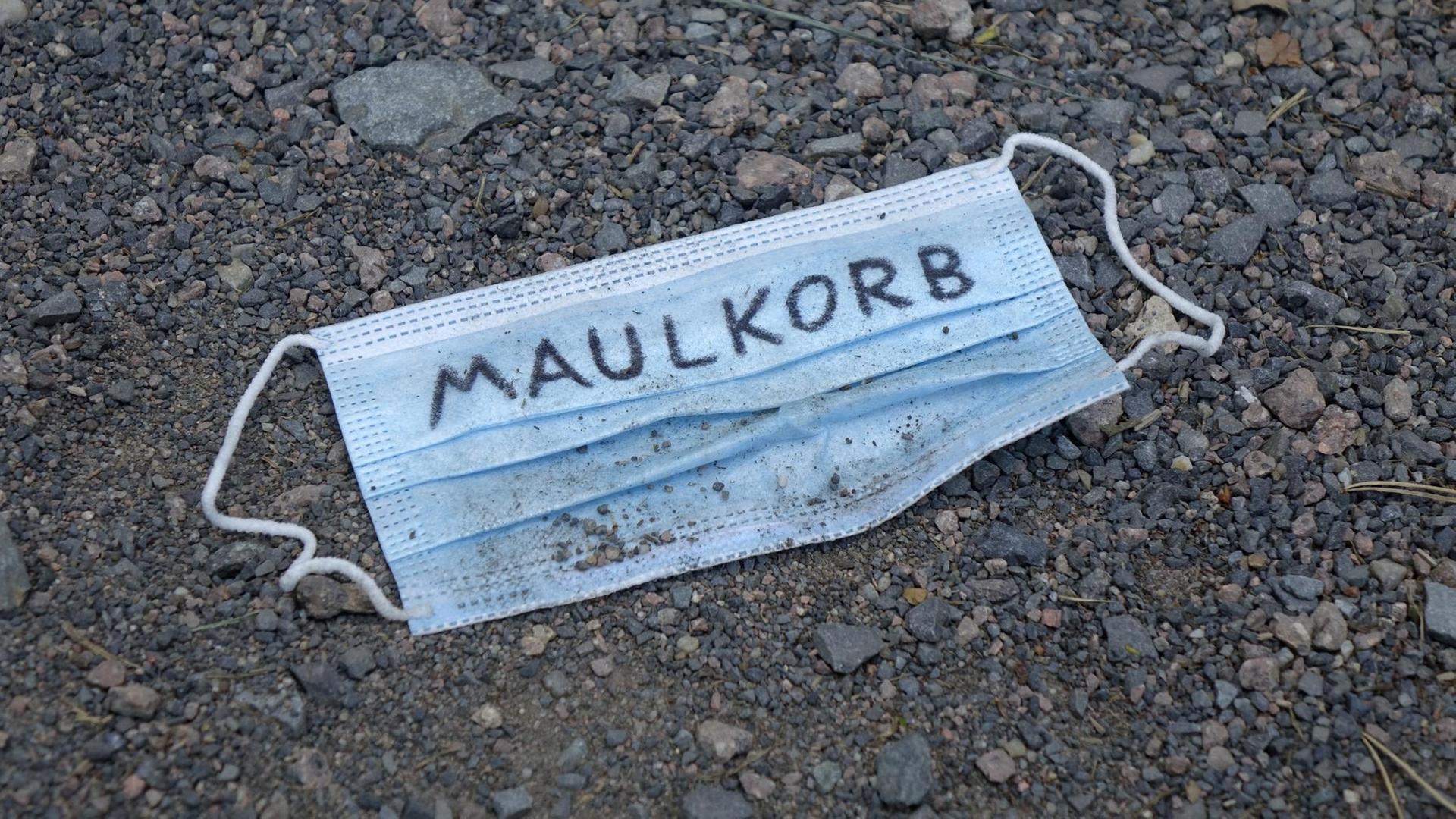 Auf einem Mundschutz steht der Schriftzug Maulkorb. Auf einem Mundschutz steht der Schriftzug Maulkorb.