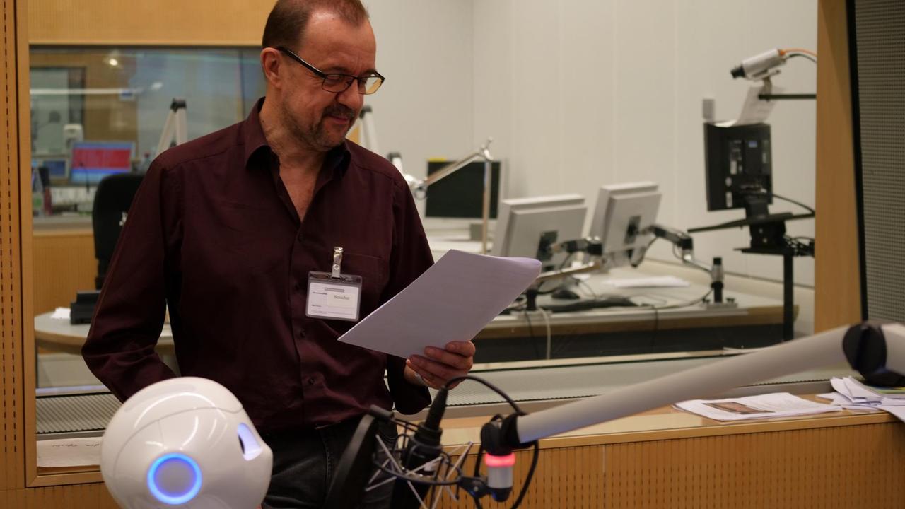 Ein Mann und ein kleiner, weißer Roboter stehen im Radiostudio Ein Mann und ein kleiner, weißer Roboter stehen im Radiostudio