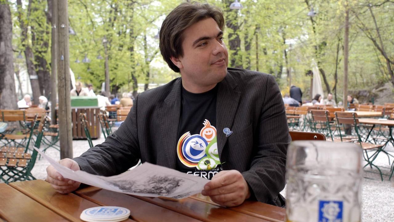 Moritz Eggert hat auf dem Foto von 2006 schwarze Haare, trägt ein dunkles Sakko und darunter ein Fanshirt mit dem Maskottchen der Fußball-WM 2006. Moritz Eggert hat auf dem Foto von 2006 schwarze Haare, trägt ein dunkles Sakko und darunter ein Fanshirt mit dem Maskottchen der Fußball-WM 2006.