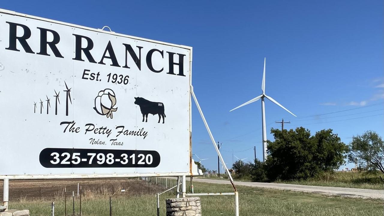 Ein großes Schild steht am Straßenrand. Darauf steht: "RR Ranch". Im Hintergrund sind Windräder zu sehen. Ein großes Schild steht am Straßenrand. Darauf steht: "RR Ranch". Im Hintergrund sind Windräder zu sehen.