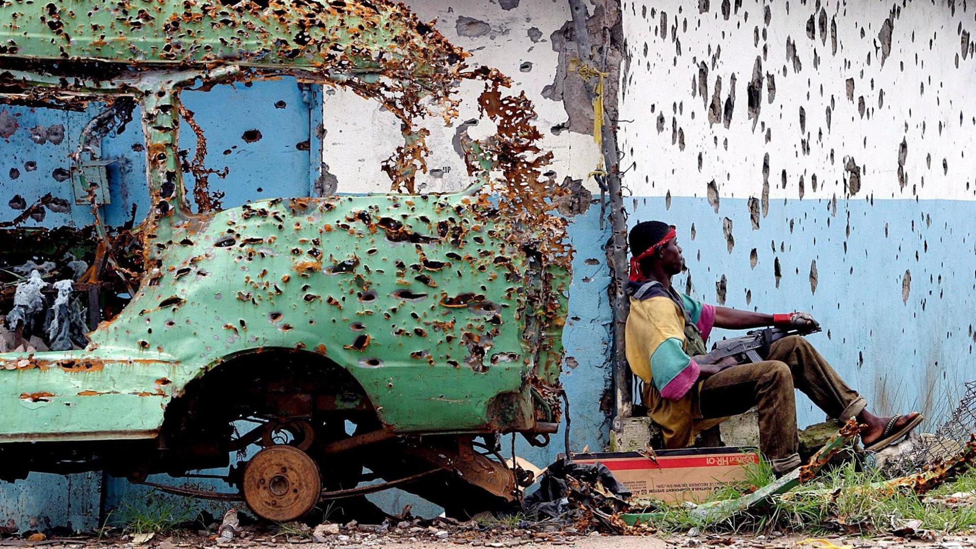 Ein Rebell der Liberians United for Reconciliation and Democracy (LURD) ruht sich während eines Waffenstillstands in Monrovia neben einem zerschossenen Fahrzeug aus