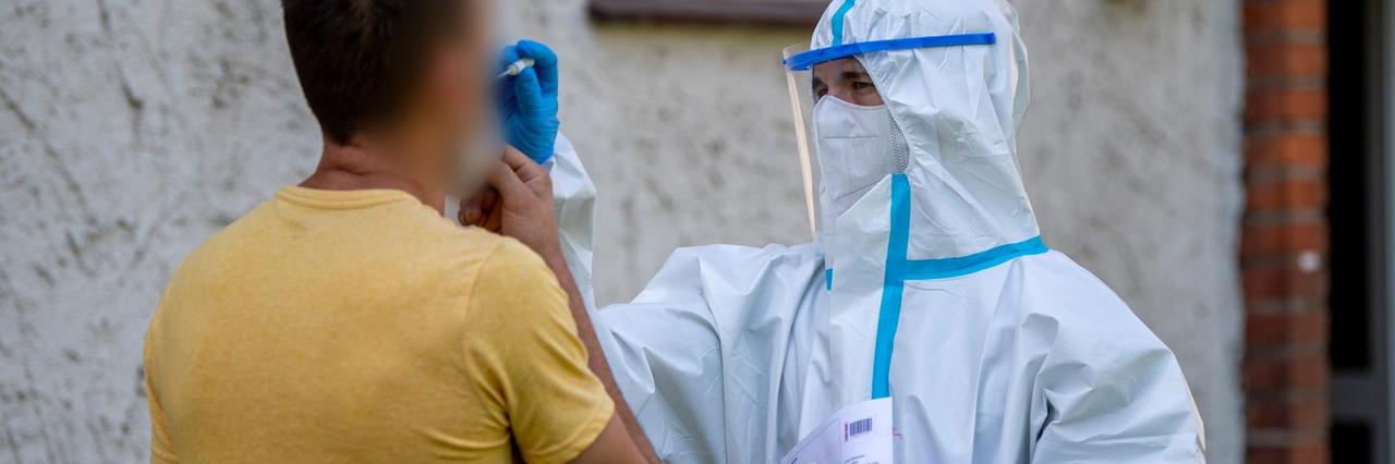 Ein Helfer vom Deutschen Roten Kreuz (DRK) nimmt vor einem Haus bei einem Mann einen Abstrich vor. 40 mobile Testteams sind unterwegs, um Angestellte der Firma Tönnies zu Hause in ihrer Quarantäne aufzusuchen. Sie überprüfen, ob diese dort anzutreffen sind und testen auch die Menschen, die mit ihnen in einem Haushalt leben. Ein Helfer vom Deutschen Roten Kreuz (DRK) nimmt vor einem Haus bei einem Mann einen Abstrich vor. 40 mobile Testteams sind unterwegs, um Angestellte der Firma Tönnies zu Hause in ihrer Quarantäne aufzusuchen. Sie überprüfen, ob diese dort anzutreffen sind und testen auch die Menschen, die mit ihnen in einem Haushalt leben.