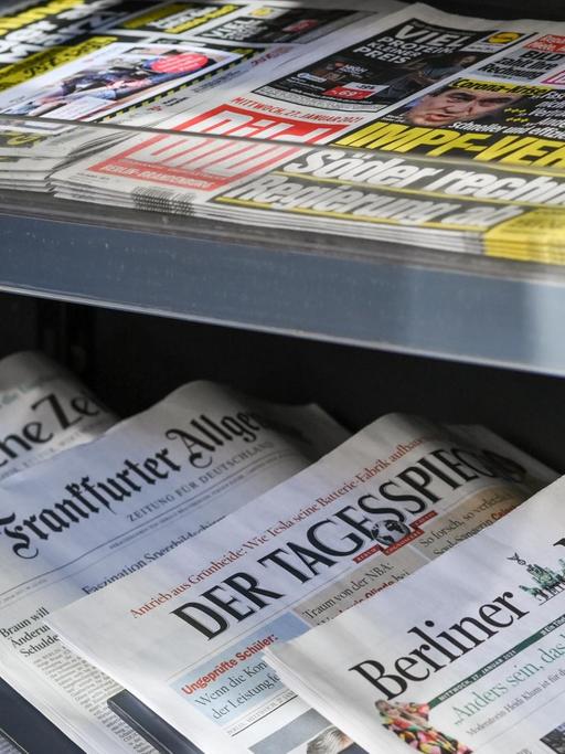 Zeitungen liegen in einer Auslage in einem Zeitschriftenladen.