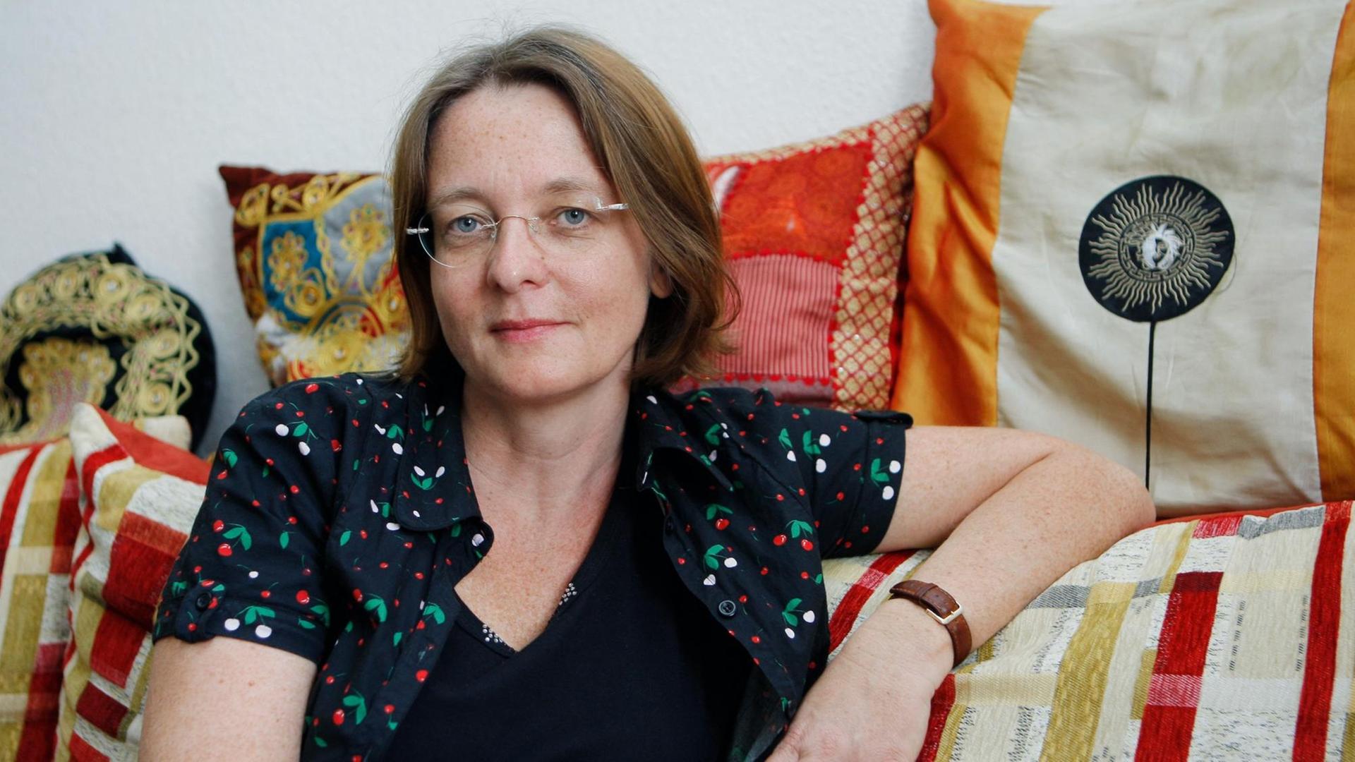 Die Schriftstellerin Grit Poppe auf einem Sofa mit bunt gemusterten Kissen.