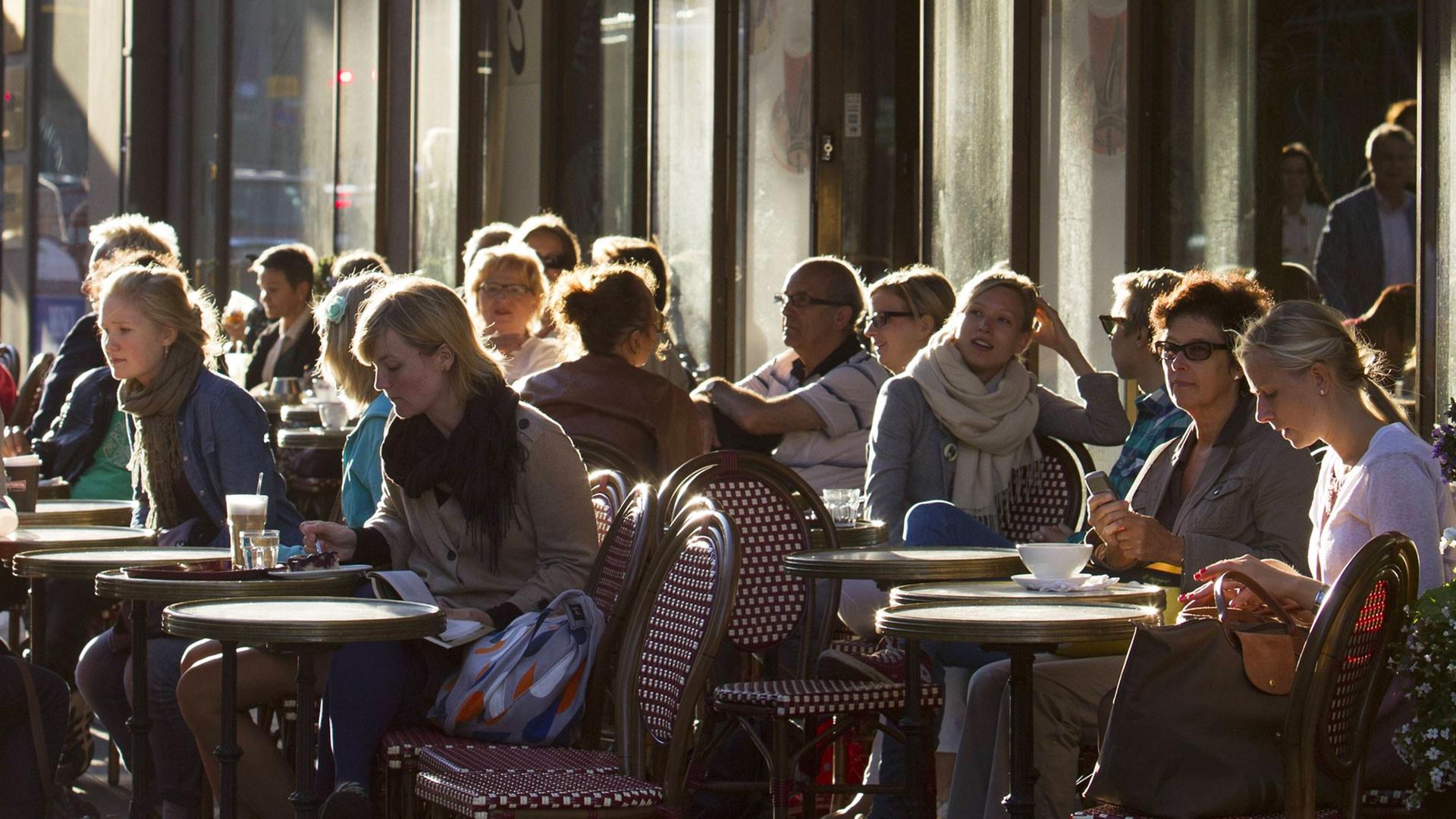 Menschen sitzen in einem Straßencafe in der finnischen Hauptstadt Helsinki Menschen sitzen in einem Straßencafe in der finnischen Hauptstadt Helsinki