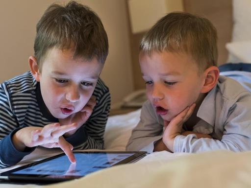Zwei Kinder beschäftigen sich mit einem iPad.