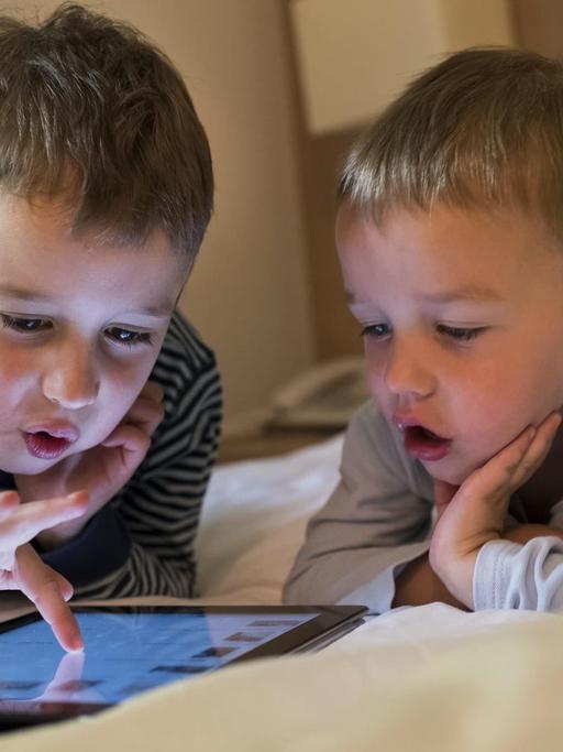 Zwei Kinder beschäftigen sich mit einem iPad.