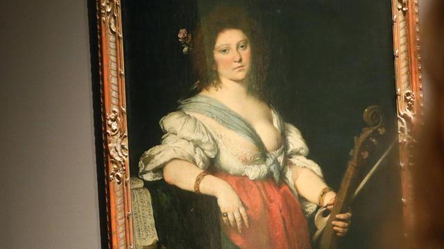 Gemälde "Die Gambenspielerin" von Bernarndo Strozzi. Sie hält eine Gambe und einen Bogen in der linken Hand, sie trägt ein rot-weißes Mieder-Kleid mit einem tiefen Ausschnitt, ihre linke Brust ist nahezu ganz entblößt