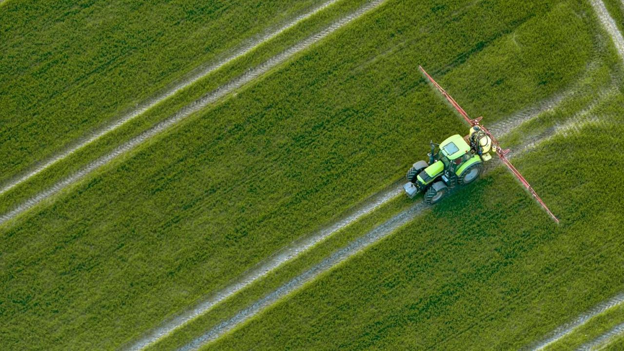 Luftaufnahme eines Traktors, der Pestizide über ein Feld versprüht Luftaufnahme eines Traktors, der Pestizide über ein Feld versprüht
