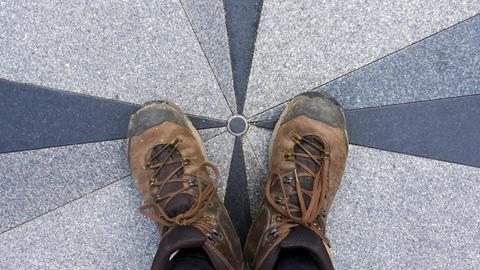 Ein Paar Füße in Wanderstiefeln stehen auf der geographischen Mitte Europas in Purnuskes, Litauen.|