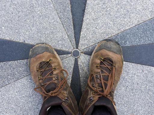 Ein Paar Füße in Wanderstiefeln stehen auf der geographischen Mitte Europas in Purnuskes, Litauen.|