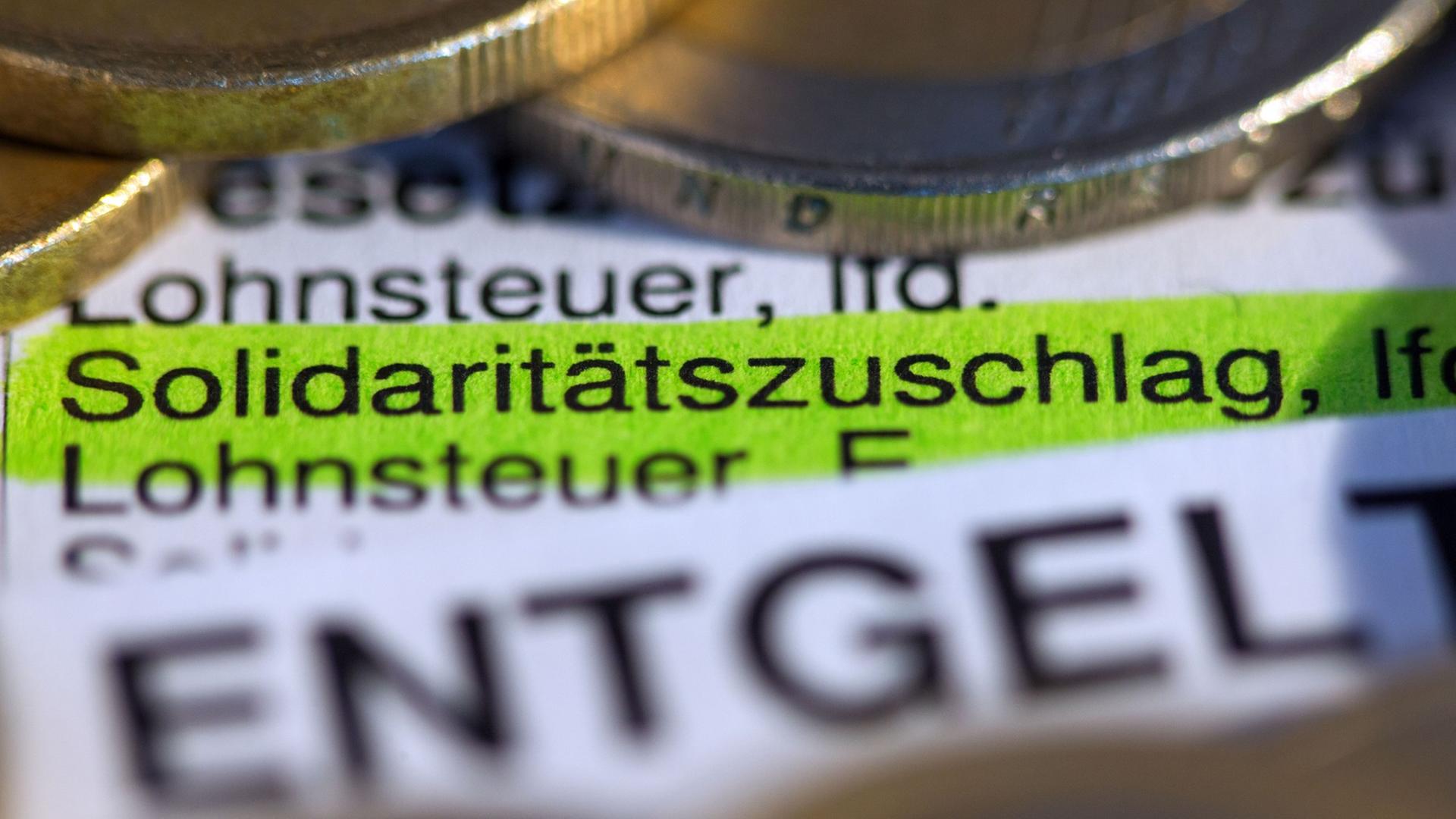 Schriftzug "Solidaritätszuschlag" auf einer Lohnabrechnung, drumrum Euromünzen.