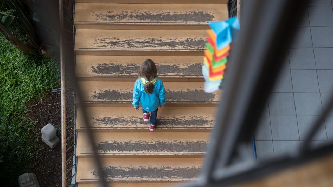Ein Mädchen geht eine Schultreppe hinauf, von der der Farbe abblättert.